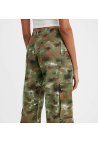 Zielone spodenki cargo w kamuflażu, wykonane z bawełny. Charakteryzują się wieloma kieszeniami, luźnym krojem oraz teksturowanym materiałem z brązowymi i szarymi akcentami.