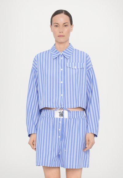Camicia button-up a righe blu e bianche, accorciata, con colletto e taschino, abbinata a pantaloni corti coordinati con elastico in vita e dettaglio del logo.