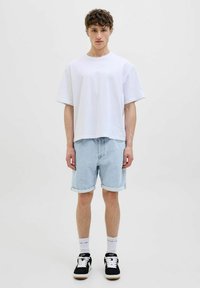 Tricou alb din bumbac și pantaloni șort din denim de culoare albastră deschisă, cu margini răsucite; adidași negri cu accente albe și șosete cu model.Ținută simplă, casual.