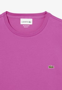 Camiseta de algodón Pima de color púrpura con cuello redondo y un pequeño logo de cocodrilo Lacoste en el lado izquierdo del pecho. Diseño de ajuste regular.