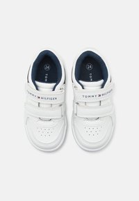 Bílé tenisky s koženým svrškem, tmavě modrou podšívkou a dvojicí suchých zipů. Jsou vybaveny perforovaným špičkou a logem "TOMMY HILFIGER". Velikost 24.