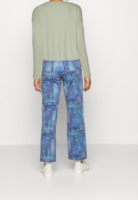 Ljusgrön stickad tröja, blå mönstrade byxor med ögon och text, samt vita sneakers med svart logga på hälen.