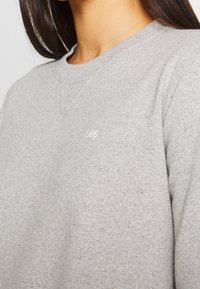 Felpa grigia chiara realizzata in tessuto morbido, caratterizzata da un colletto a girocollo e un piccolo logo bianco sull'area sinistra del petto.