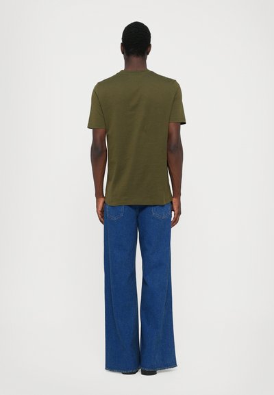 Tricou cu maneci scurte de culoare verde măsline, asociat cu blugi lungi de denim albastri, cu croi larg. Tesătura pare fină, cu cusături vizibile și buzunare.