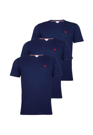 Tři námořnicky modré trička s výstřihem do V a krátkými rukávy naskládaná na sobě, každé s malým červeným vyšívaným logem na levé straně hrudi.