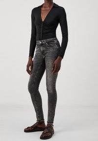 Body negro de manga larga con escote pronunciado y cierre de botones, combinado con jeans ajustados grises y sandalias negras con tiras.