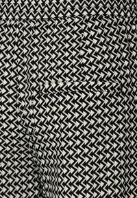 Svart och vit mönstrad tyg med en geometrisk zigzag-design, med en synlig fickdetalj. Texturerat och slätt material.