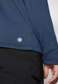 Camicia a maniche lunghe blu navy realizzata in un tessuto liscio e traspirante, con un logo circolare vicino all'orlo e pantaloni neri con dettagli con zip.