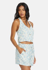 Lichtblauw cropped tanktop met bloemenpatronen en twee knopen, gecombineerd met bijpassende shorts met een koord en zijzakken.