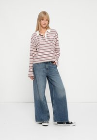 Polo à rayures à manches longues avec un col blanc, associé à un jean bleu clair à jambes larges et des baskets noires.