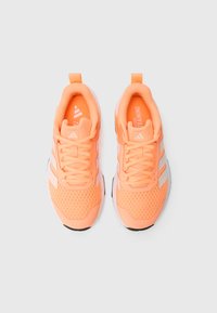 Sportowe trampki w jasnym pomarańczowym kolorze z siateczkową, teksturowaną powierzchnią, białymi akcentami oraz płaskimi sznurowadłami. Posiadają pętelkę z tyłu na pięcie.