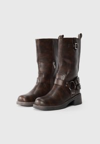 Botas de cuero marrón hasta la mitad de la pantorrilla con puntera redondeada, cremallera lateral, hebillas ajustables y tacón bajo apilado. Acabado texturizado con acentos oscuros.