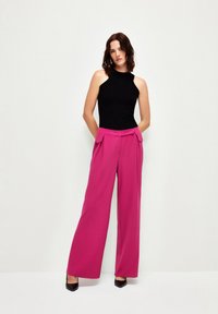 Haut sans manches noir à côtes associé à un pantalon large taille haute rose avec poches latérales et lignes épurées. Escarpins noirs à bout pointu.