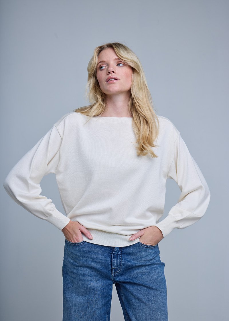 Pull surdimensionné de couleur crème avec manches longues et poignets côtelés, associé à un jean en denim bleu. Texture douce et coupe décontractée.