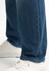 Granatowe dżinsy typu loose fit z wykończonym dołem oraz białe sneakersy o gładkiej fakturze i sznurowanym designie.