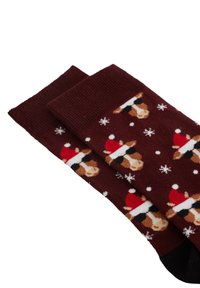 Mörkröda strumpor med ett upprepande mönster av kor som bär tomteluva och solglasögon, omgivna av vita snöflingor.