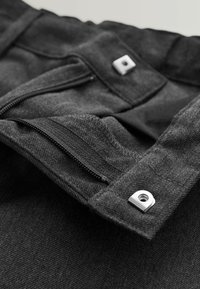 Mørkegråt stof med en delvist åben lynlås og to sølvfirkantede trykknapper på et beklædningsstykke.