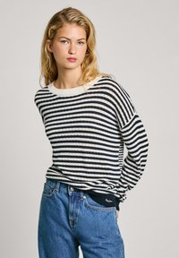 Pull marinière bleu marine et blanc avec un col côtelé et une coupe décontractée, associé à un jean bleu taille haute. Tricot texturé visible.