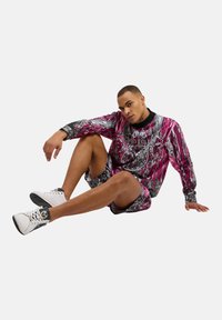 Fargerik mønstrete genser og shorts i nyanser av rosa, svart og grått; kombinert med hvite sneakers med svart aksent.