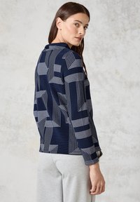 Marineblauer Pullover mit geometrischem weißen Linienmuster, langen Ärmeln und lockerer Passform. Weiche Textur mit geripptem Abschluss.