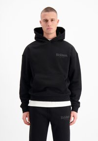 Zwarte hoodie met een zachte textuur, voorzien van een voorkantzak en een logo op de borst. Gecombineerd met zwarte joggers.