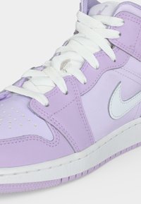 Μωβ και λευκό high-top παπούτσι Nike με λευκά κορδόνια και διάτρητο μπροστινό μέρος, που δείχνει το λογότυπο στο πλάι και την υφή στην άκρη της σόλας.