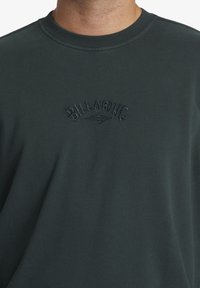 Mörkgrön tröja med rund hals, med ett texturerat broderat logotyp i en kontrasterande nyans. Mjukt tyg med en avslappnad passform.