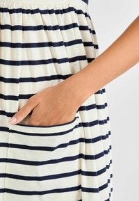 Gestreepte jurk in marineblauw en crème, met een gekruiste taille en een zijzak. Zachte katoenstof met een casual pasvorm.
