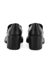 Par de zapatos de cuero negro de tacón grueso vistos desde atrás, mostrando tacones anchos y detalles de costura suave.