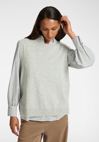 Lichtgrijze gebreide trui met een hoge hals, over een zwart-wit gestreepte blouse met kraag. Ribgebreide zoom en ballonmouwen.