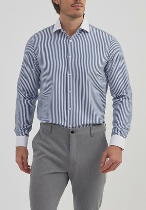 Chemise habillée rayée bleue et blanche pour homme avec manches longues, col blanc contrastant et boutonnière. Associée à un pantalon gris.