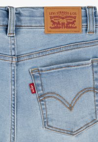 Ljusblå denimjeans med en läderlapp som har "Levi Strauss & Co." och en röd tab. Karakteristisk sömnad bildar en dubbel båge på bakfickorna.