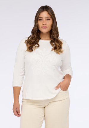 Camiseta de manga larga blanca con escote redondo y un patrón decorativo en relieve en la parte delantera. Tejido suave con un dobladillo ligeramente curvado.