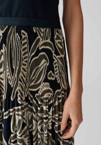 Gonna plissettata con una base blu navy scuro e grandi motivi floreali beige. La vita scura e i dettagli in tessuto testurizzato creano profondità e interesse visivo.