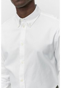 Chemise blanche en coton à boutons, avec un col pointu, une texture subtile et des boutons jaunes le long de la patte de boutonnage.