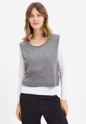 Grauer, kurzer Strickpullover mit rundem Ausschnitt, über einem weißen Langarmshirt, kombiniert mit schwarzen Hosen. Weiche Textur und einfaches Design.