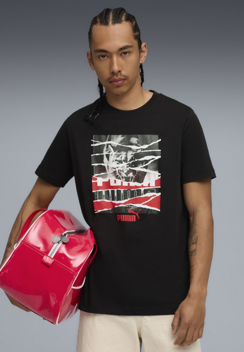 Sort bomulds T-shirt med grafisk print med røde og hvide accenter. Rød blank taske med en sølv lynlås, der holdes i hånden.