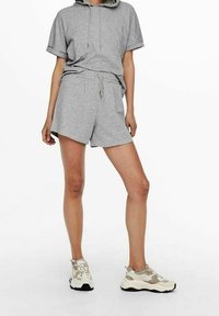 Grå kortärmad hoodie och matchande shorts i ett mjukt tyg. Outfiten har dragsko och avslappnad passform, i kombination med beige sportskor.