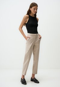 Un débardeur noir à côtes associé à un pantalon beige taille haute. Le pantalon présente une fermeture à bouton et des poches latérales. Des mocassins noirs sont portés avec l'ensemble.