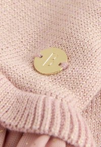 Svijetloružičasta pletenina s suptilnim metalnim nitima. Ima rebrastu teksturu i zlatni okrugli logotip s 'B' u prilogu.