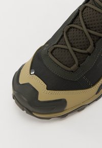 Czarno-oliwkowe buty trekkingowe z teksturowaną siateczką, wzmocnionym palcem i gumową podeszwą. Posiadają sznurówki z metalowymi akcentami.