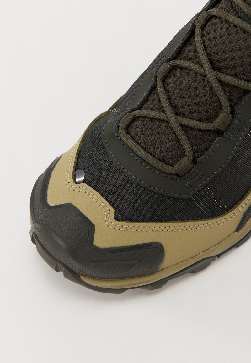 Black and olive green hiking shoe with a textured mesh upper, reinforced toe, and rubber outsole. Features lacing with metal accents.