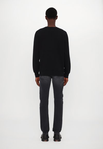 Sudadera negra de mangas largas con cuello redondo, combinada con jeans gris oscuro. El calzado es negro, con una suela texturizada.
