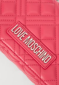 Quilted rosa syntetisk handveske med et sølvfarget "LOVE MOSCHINO" logo-merke og myk tekstur med synlige sømdetaljer.
