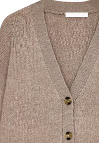 Beige stickad cardigan med V-hals, med tre svarta knappar och en texturerad yta. Anmärkningsvärda detaljer inkluderar ribbade kanter.