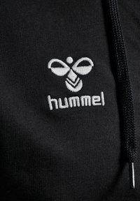 Zwarte hoodie met een witte geborduurde logo met een symmetrisch ontwerp en het woord "hummel." Treklus met een zilveren metalen accent.