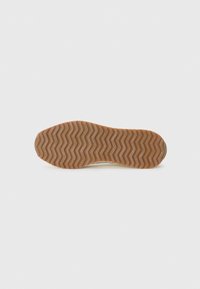 Semelle de chaussure en caoutchouc marron avec un motif de bande de roulement en zigzag, vue de dessous sur un fond clair et uni. Pas de personnes ni d'autres objets.