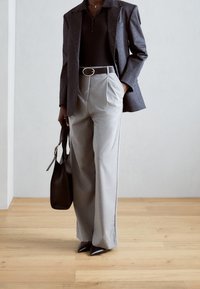 Grå skräddarsydda byxor med hög midja, i kombination med en mörk åtsittande skjorta och en blazer i ränder. Svarta spetsiga klackar och en svart väska.