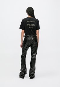 Μαύρο μπ�λουζάκι, από πίσω, με την επιγραφή «Sea breezy, PINKO, EASY!» σε χρυσό. Συνδυασμένο με λαμπερό μαύρο παντελόνι από τεχνητό δέρμα, με λεία υφή.