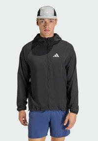 Μαύρο ελαφρύ τρέξιμο μπουφάν με πλήρη φερμουάρ, κουκούλα και ανακλαστική λεπτομέρεια λογότυπου. Διαθέτει ελαστικές μανσέτες και απαλή υφή.